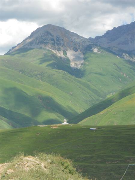Small white church alone on green hills, rocky peaks among clouds