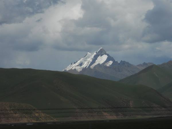 Snow-capped peak behind green hills and grey clouds, shot from train window