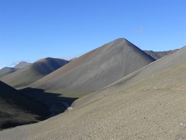 Road climbing through barren grey mountains under clear blue sky