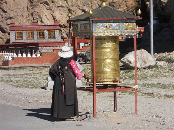 Pilgrim in traditional long robe spins the golden prayer wheel