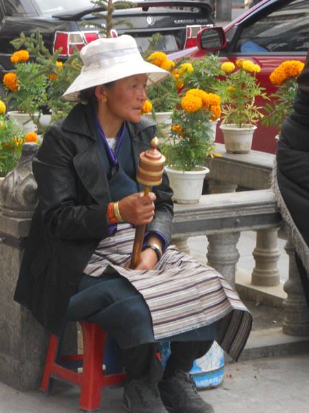 Woman in white hat sitting on red stool among marigold pots