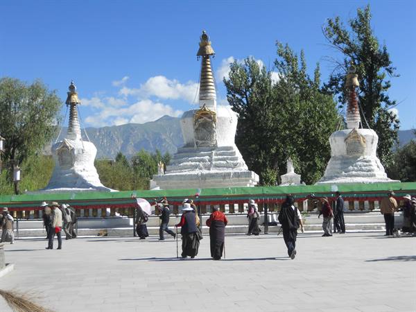 Pilgrims walking around three white stupas with golden spires, Lhasa