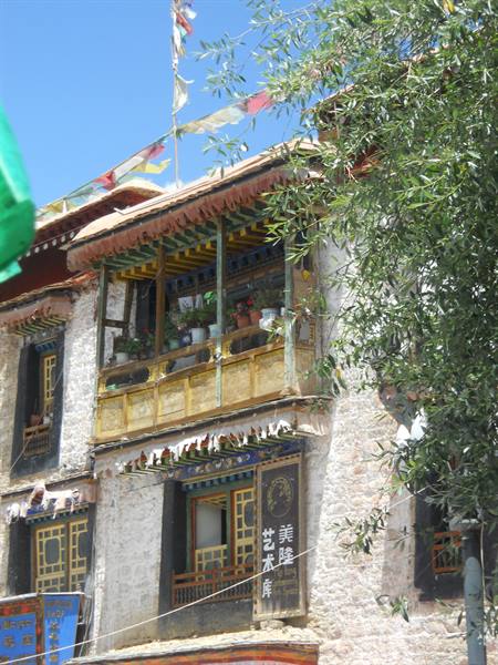 Painted wooden balcony on stone facade with prayer flags, Lhasa
