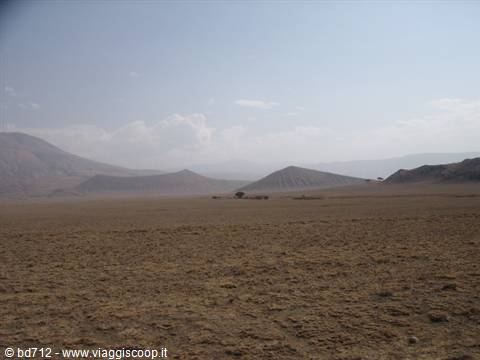 Arid plain with eroded volcanic cones under a hazy cloudy sky
