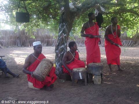 Men in red robes play wooden drums beneath a large tree