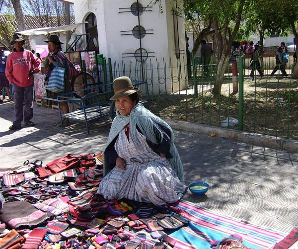 Woman in hat and shawl selling colorful woven textiles on a plaza ground
