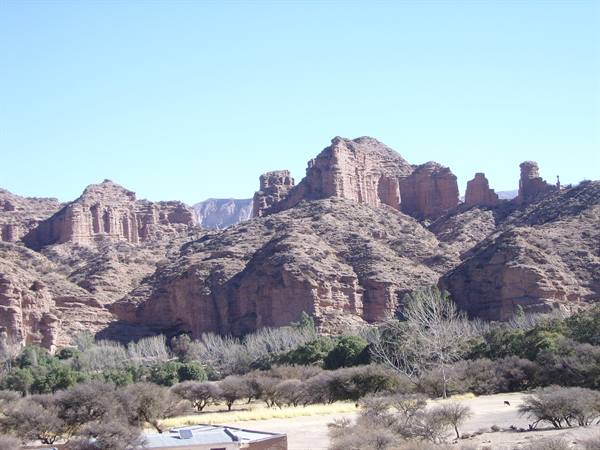 Red rock formations above scattered trees and a grey roof, blue sky