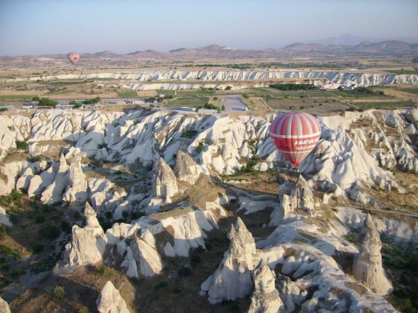 Red hot air balloon flying over Cappadocia rock formations