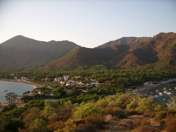 Village by the bay among green hills, boats at moorings, evening light