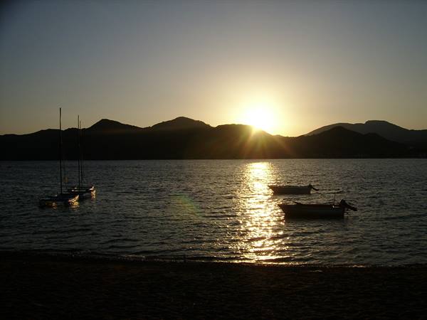 Anchored boats offshore, the low sun reflects on the water before the mountains