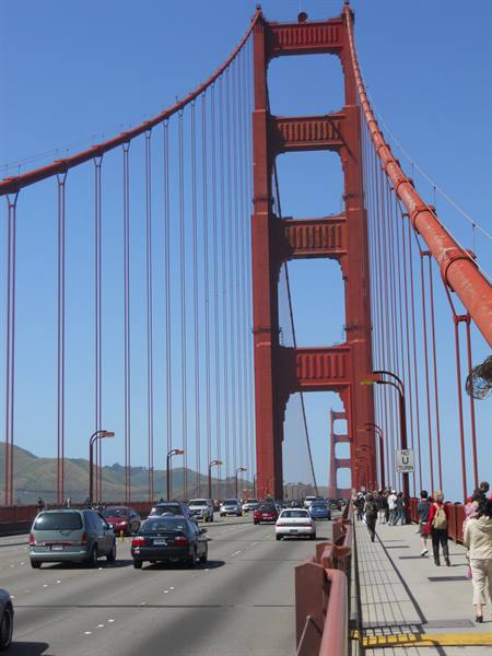 Tourists walk along the Golden Gate Bridge sidewalk beside moving traffic