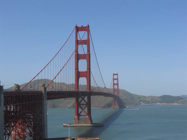 Red tower of the Golden Gate Bridge over the bay, green hills, blue sky