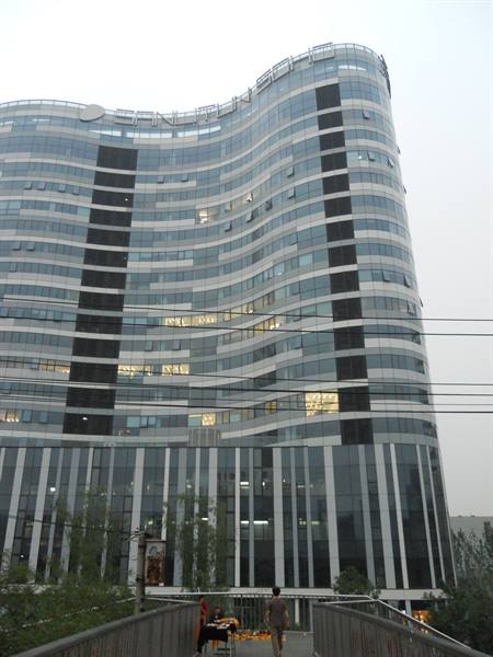 Pedestrian on walkway before curved glass skyscraper, overcast grey sky