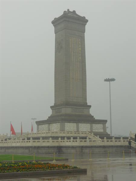 Stone stele in fog on a square with flowerbeds and red flags, Tiananmen Square
