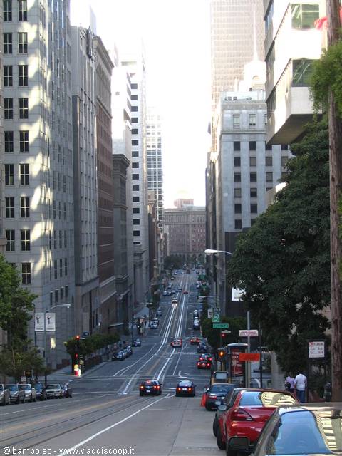 Steep street between skyscrapers with cars passing, morning light