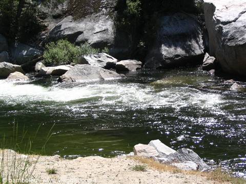 River rapids among granite boulders and sand, sunlight sparkling on water