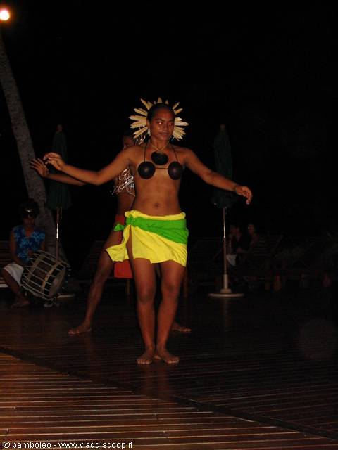Dancer in yellow and green skirt performs at night on wooden floor