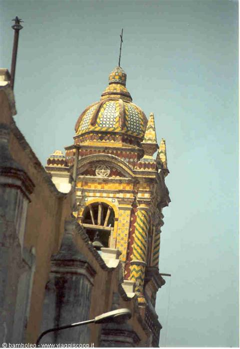 Baroque bell tower with yellow and green tiles, blue sky, bell in archway