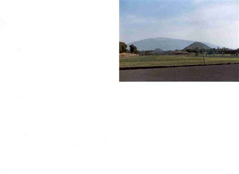 Asphalt road toward green fields and mountain in hazy distance