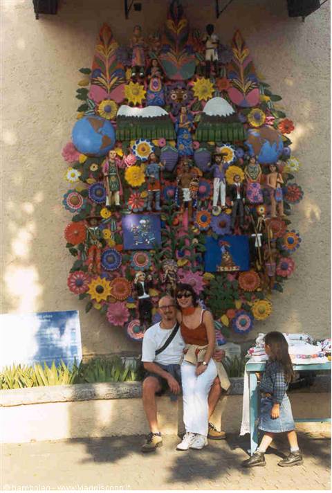 Couple sitting before a colorful mosaic of flowers and dolls, girl nearby