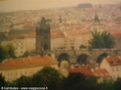 Charles Bridge blurs among Prague's red rooftops under a grey sky