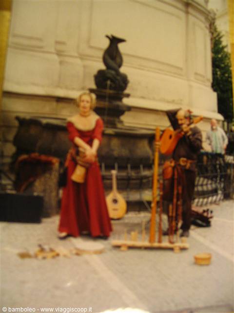 Medieval street musicians in costume play by a dolphin fountain, lutes on the ground