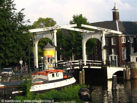 White wooden drawbridge over canal, moored boat and brick houses nearby