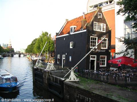 Black wooden house along an Amsterdam canal, with boat and outdoor café tables