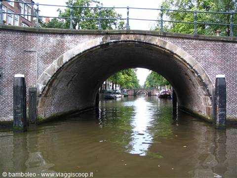 Brick bridge arch over Amsterdam canal, boats and houses beyond