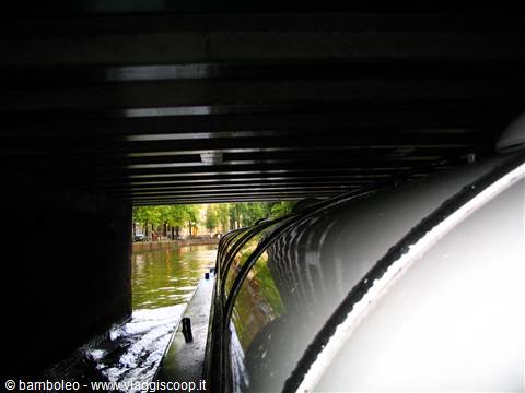 Tour boat gliding under a low canal bridge in Amsterdam
