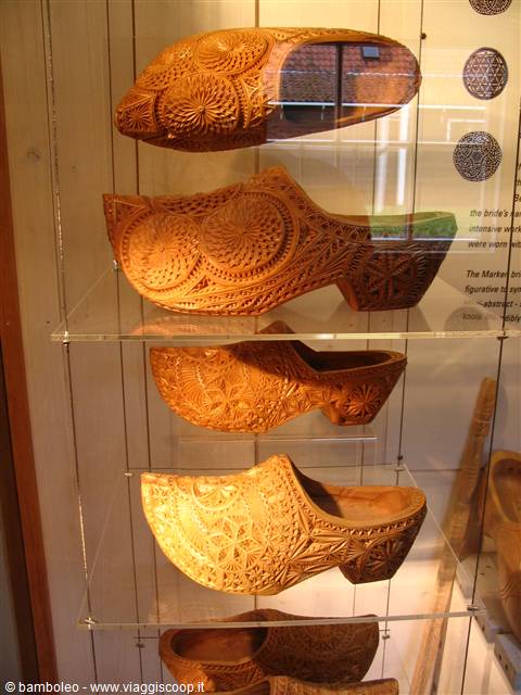Intricately carved wooden clogs displayed in a lit museum glass case