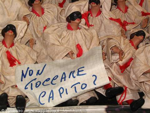 Dolls with white hoods and black masks, handwritten sign among them