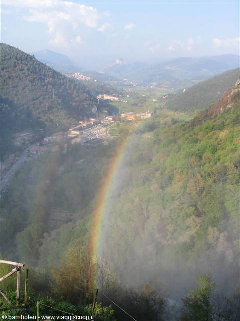 Rainbow over waterfall mist, green woods and valley town with mountains