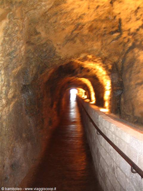 Tunnel carved in rock with raised walkway and warm lights