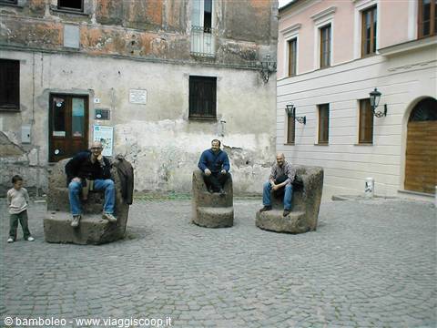 Cobbled square with giant stone chairs, men sitting among old buildings