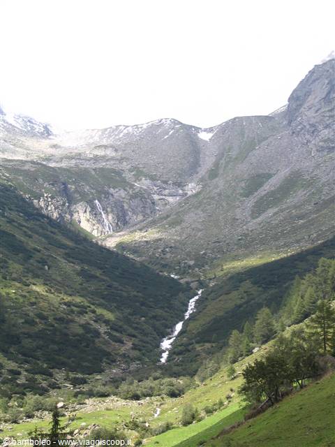 Waterfall cascades down rocky slopes toward green alpine meadows