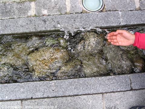 A hand touches water flowing over stones in a granite channel