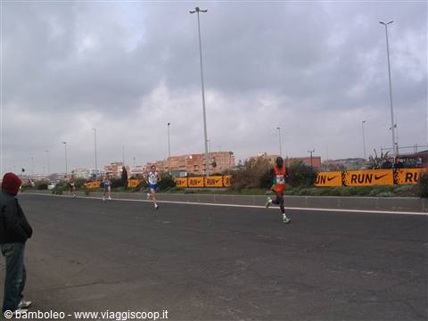 Marathon runners on a city road, yellow Nike banners, cloudy sky