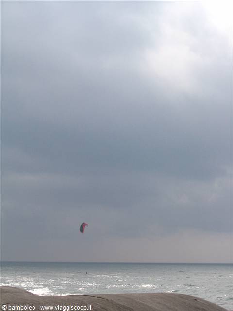 Kitesurf kite over choppy sea, gray cloudy sky, rocks in foreground