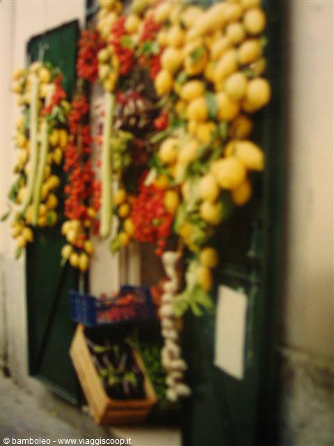Green kiosk hung with lemons, cherry tomatoes and garlic, crates of fresh produce