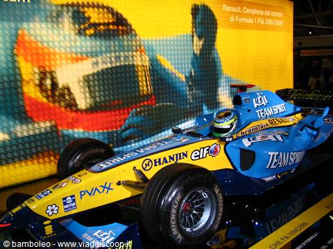 Blue and yellow Renault F1 car displayed indoors, giant driver banner behind