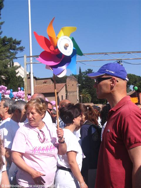 Woman holds multicolored pinwheel on a stick, crowd in pink shirts under sun