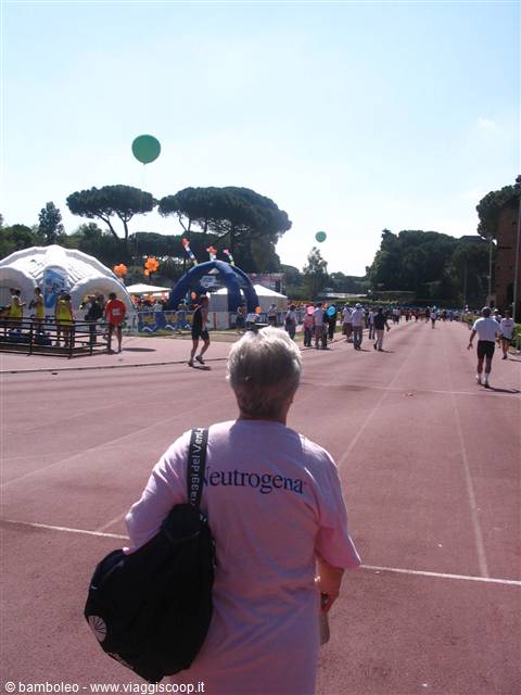 Woman in pink Neutrogena shirt walks on red track among tents and balloons