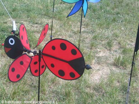 Red ladybug-shaped garden spinner with black wings stuck in the grass