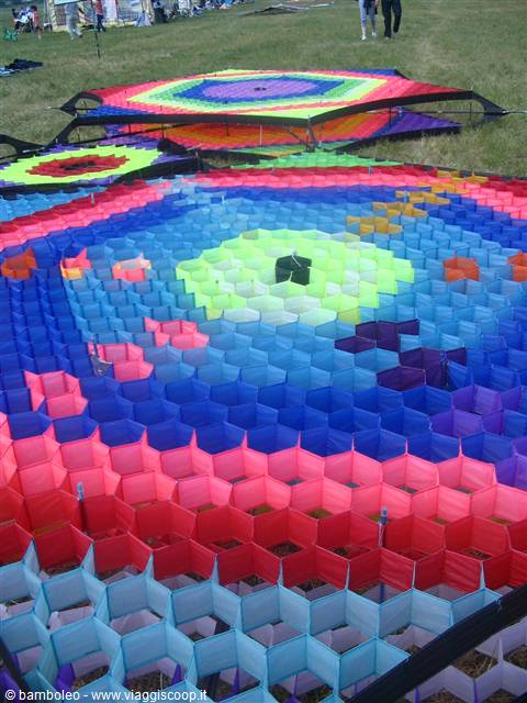 Giant colorful hexagonal kites laid out on the grass, people nearby