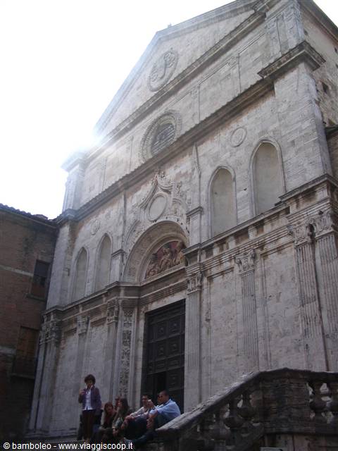 Tourists sitting on the steps of the travertine facade of San Francesco church in Montepulciano