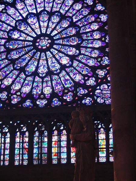 Stained glass rose window of Notre-Dame behind a stone statue