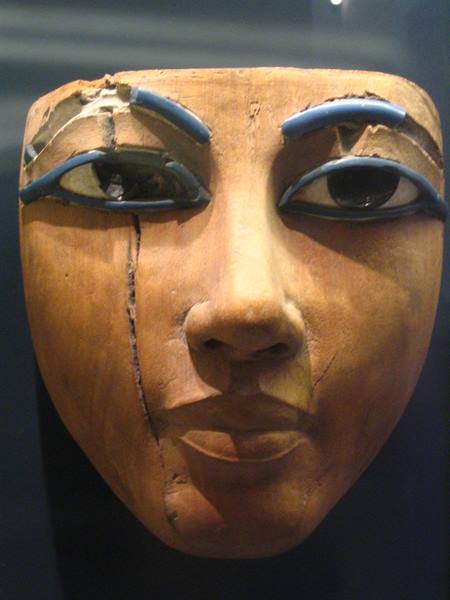 Wooden funerary mask with blue glass eyes, displayed in a museum case