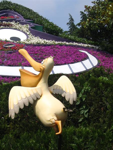 White pelican statue among purple flowers and green hedges