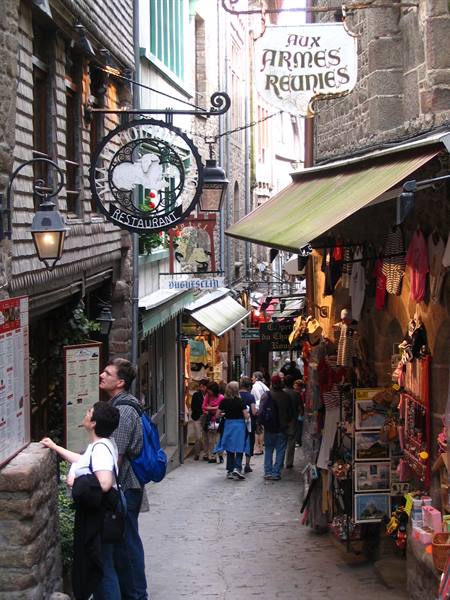Tourists in Mont-Saint-Michel narrow street among restaurant signs and souvenir shops